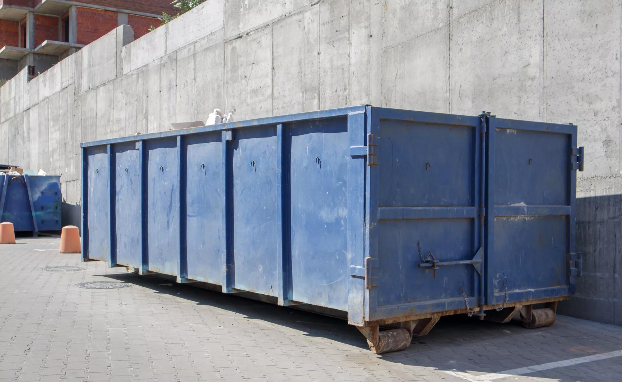Metal durable blue industrial trash bin for outdoor trash at construction site. Large waste basket for household or industrial waste. A pile of waste